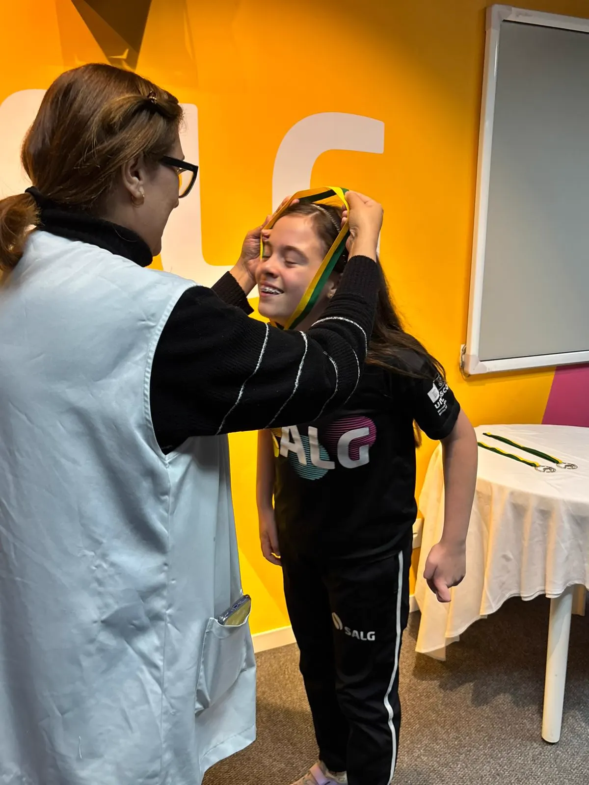 Professora colocando a medalha da Olimpíada Canguru em uma aluna